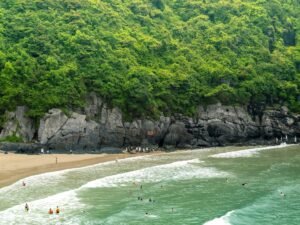 A beautiful summer beach scene with a lush cliff and people enjoying the waves.